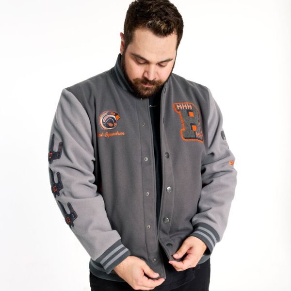 Show your allegiance in stealth style with our Loungefly COLLECTIV STAR WARS™ Rebel Alliance™ VRSITY Jacket. This fashionable jacket features discreet callouts to your favorite fandom. Elevated details, such as embroidery and chenille patches, add varied textures and an elegant flair. At the top, there’s a chenille patch “R” with orange Rebel X-Wings™. Another patch at the top features the Rebel Alliance helmet, with “Red-Five” embroidered below. The sleeves are color-blocked, with chenille patches displaying the embroidered Rebel Alliance logo in orange, along with Rebel X-Wings. Custom-molded metal snaps, down the front, feature the Rebel Alliance symbol as well. Screen printing, at the pocket openings, adds a touch of color in a motif consisting of the STAR WARS logo and Rebel Alliance symbol. On the back, the embroidery in orange says “Rebel” in Aurebesh, and embossed art of the Rebel Alliance symbol makes a grand encore appearance. The Loungefly COLLECTIV STAR WARS Rebel Alliance VRSITY Jacket is made of 100% for the outer shell and lining. Other features screen printing, chenille patches, embroidery, custom-molded metal buttons, and stiped knit band. Take note of the coordinating inside lining. This jacket is an officially licensed STAR WARS product. Comes in unisex sizes S through 3X. Sizing is very specific, so please consult the size chart before purchasing.