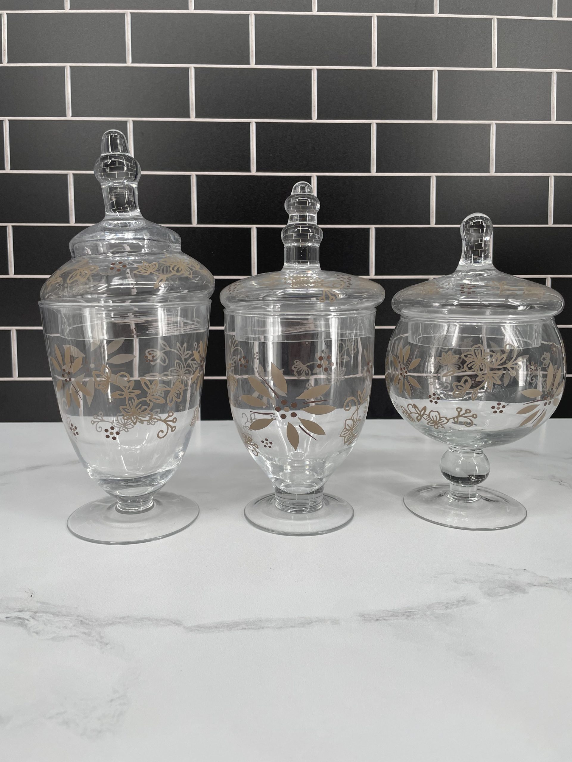 The Temp-tations Classic Set of 3 Glass Kitchen Apothecary Jars in Taupe offers a stylish and practical solution for organizing your kitchen. These elegant jars are made from durable glass, providing a clear view of their contents while adding a touch of sophistication to your countertop or pantry. The taupe color gives them a modern, neutral look that complements various décor styles. Each jar features an airtight lid to keep contents fresh and protected from moisture. Perfect for storing ingredients like sugar, flour, coffee, or even small kitchen tools, this set brings both functionality and charm to your culinary space.